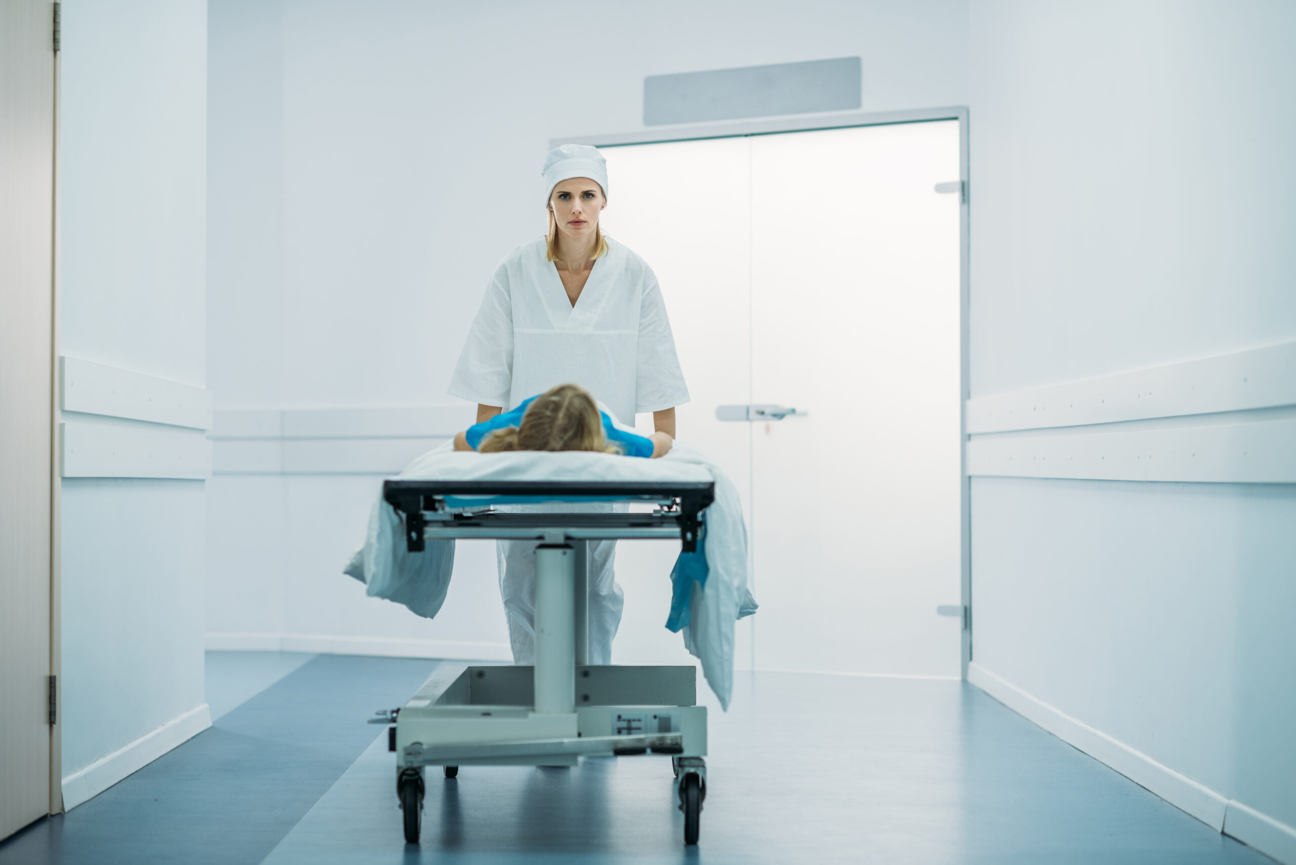 Nurse moving preschooler patient on medical stretcher in corridor